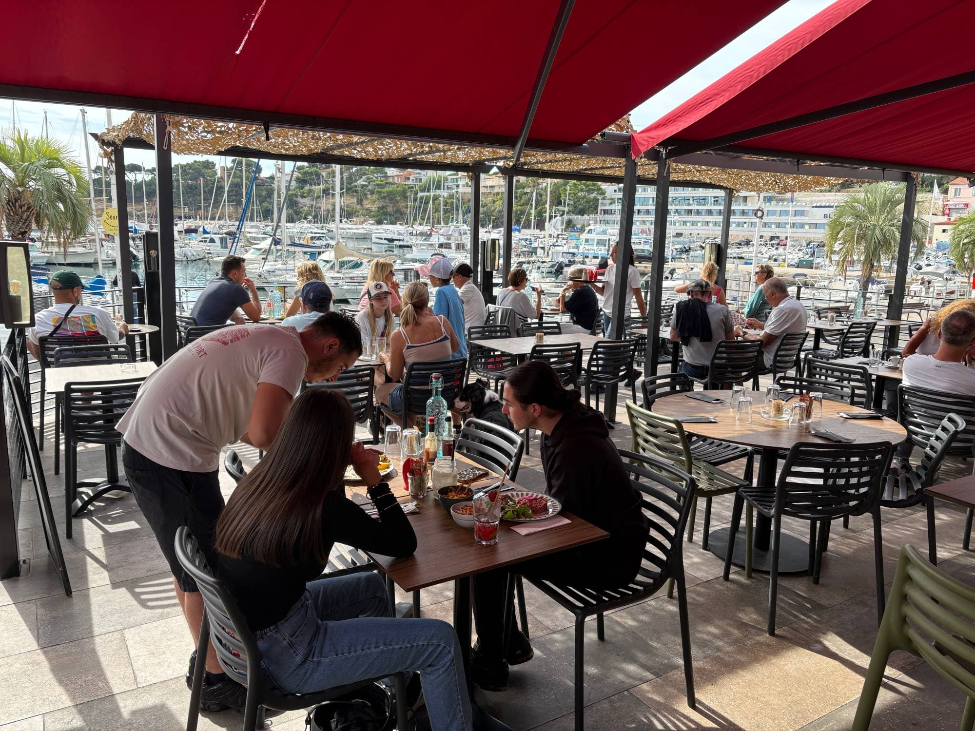 La terrasse du Café du Port sous les stores rouges, face au port de Carry-le-Rouet